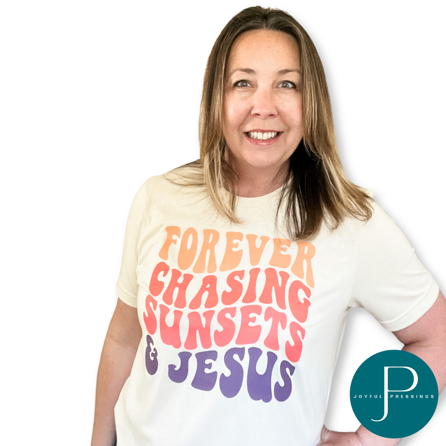 Smiling woman wearing a heather soft cream t-shirt with bold retro lettering that reads "Forever Chasing Sunsets & Jesus" in orange, coral, and purple.