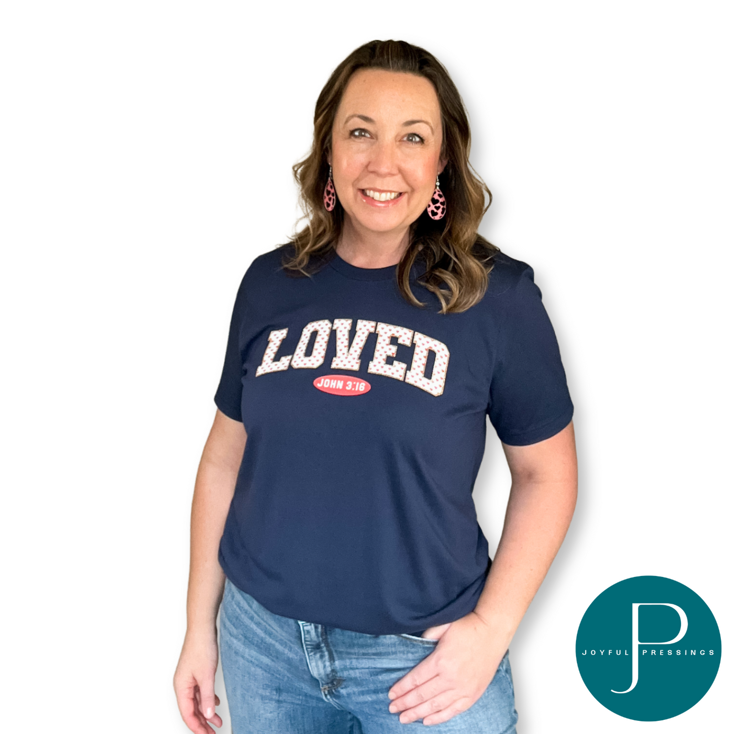 model wearing a navy blue tee with the word loved in white and adorned with pink hearts. underneath is the reference to the verse John 3:16
