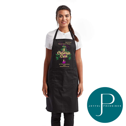 Black apron with adjustable neckline and front pockets, featuring the A Christmas Carol 2025 cast and crew logo in gold lettering, greenery accents, and a purple candle design.
