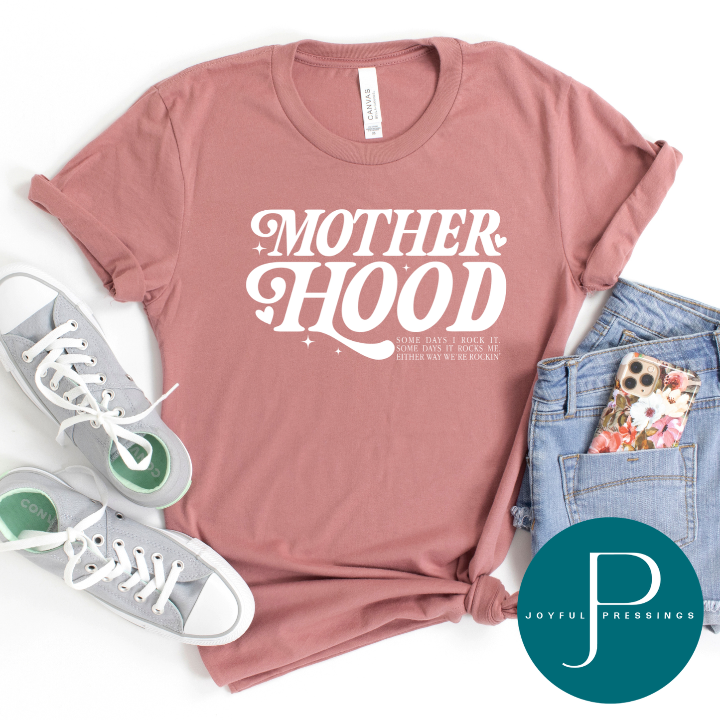 Pink t-shirt with 'MOTHERHOOD' text, sneakers, jeans, and phone case on a white background with Joyful Pressings logo.