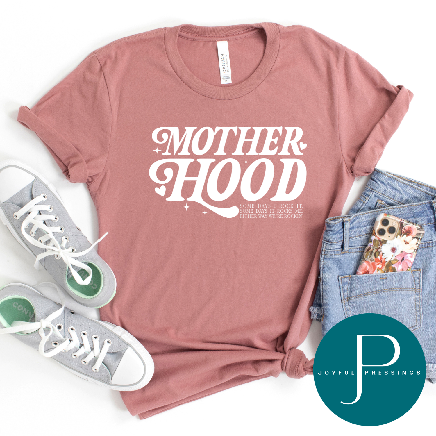 Pink t-shirt with 'MOTHERHOOD' text, sneakers, jeans, and phone case on a white background with Joyful Pressings logo.
