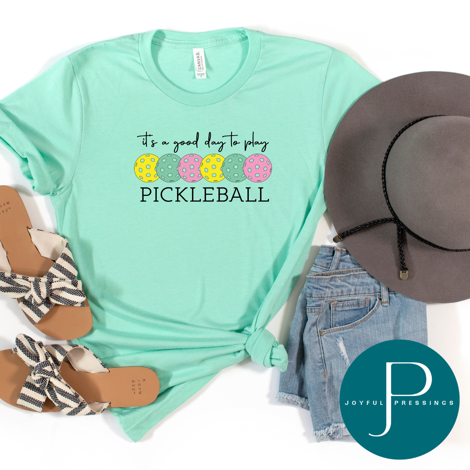 Mint green t-shirt with pickleball design, gray hat, denim shorts, and sandals on a white background with Joyful Pressings logo.
