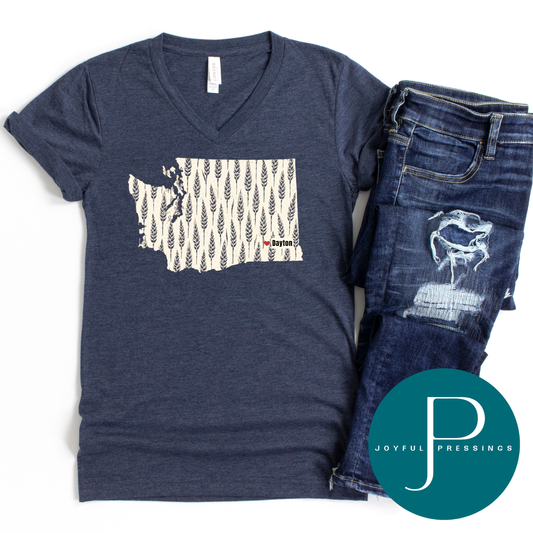 A navy blue heather V-neck t-shirt featuring a cream-colored outline of Washington state filled with a vertical wheat pattern and the text 'Dayton'.