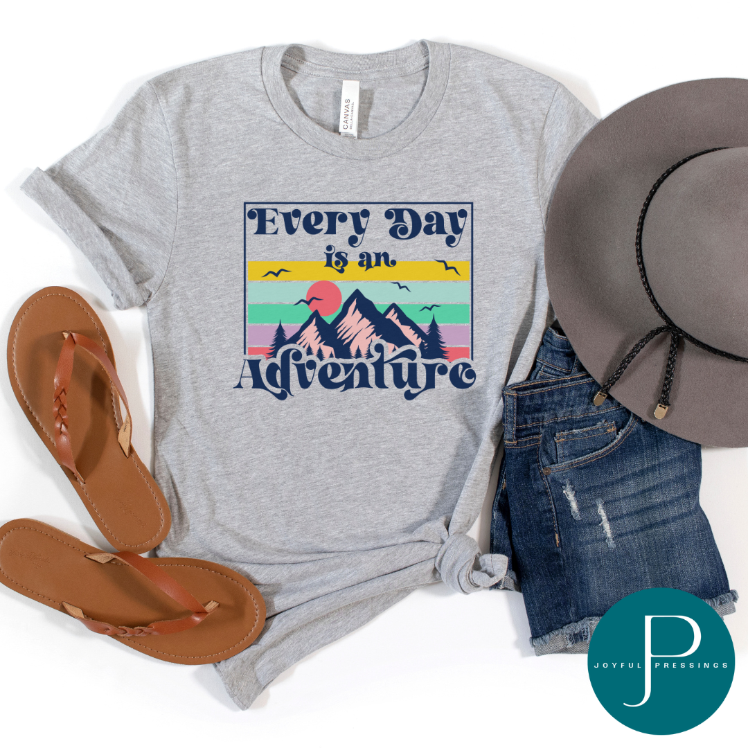 Everyday is an Adventure colorful print on a gray tee.  Displayed in a flatlay with sandals, shorts, and hat.