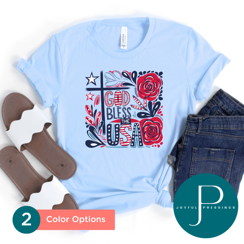Light blue t-shirt with 'God Bless the USA' design, placed on a white background with jeans and chocolate candies.