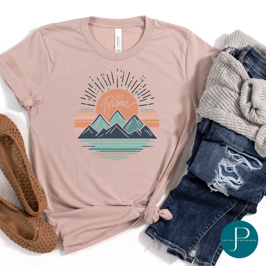 Mockup of He is Risen pink gravel t-shirt.  Features a mountain scene with a beautiful sunrise.