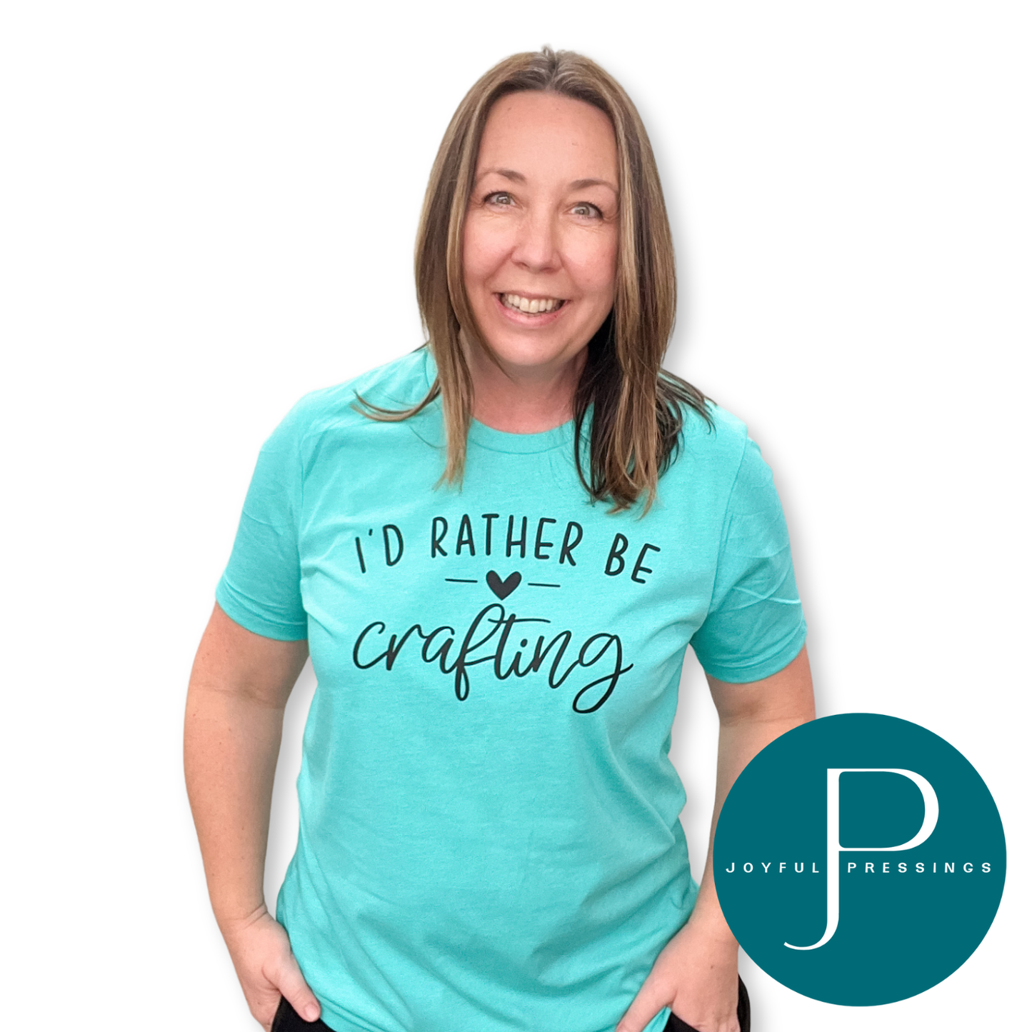 Woman wearing a heather sea green ‘I’d Rather Be Crafting’ t-shirt, smiling with hands in pockets.