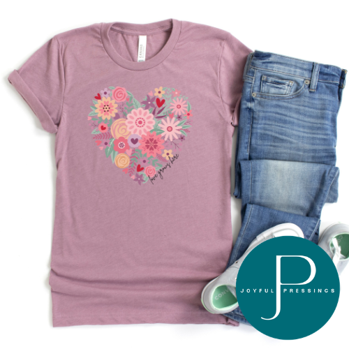 A mauve pink short-sleeve t-shirt with a colorful heart-shaped floral graphic on the chest, styled in a flat lay with blue jeans, white sneakers, and a teal circular 'JOYFUL PRESSINGS' brand overlay on a white background.