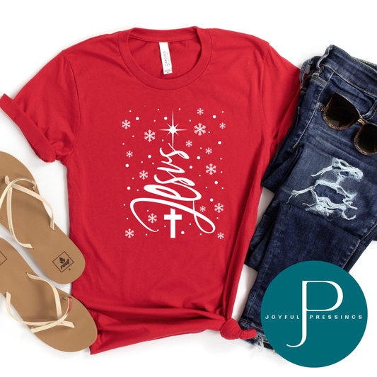 Red Bella + Canvas t-shirt with white “Jesus” Christmas tree design, snowflakes, and cross — Christian holiday shirt by Joyful Pressings.