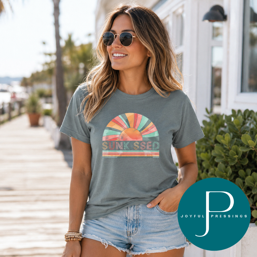Woman wearing a t-shirt with a colorful sunkissed graphic design outdoors, with 'Joyful Pressings' logo.