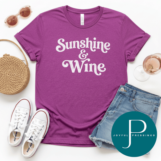 Magenta t-shirt with 'Sunshine & Wine' text, sunglasses, white sneakers, denim shorts, and a woven bag on a white background.