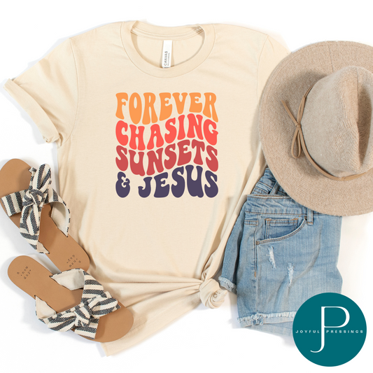 Woman wearing a heather soft cream t-shirt with the phrase "Forever Chasing Sunsets & Jesus" in bold sunset-colored lettering.