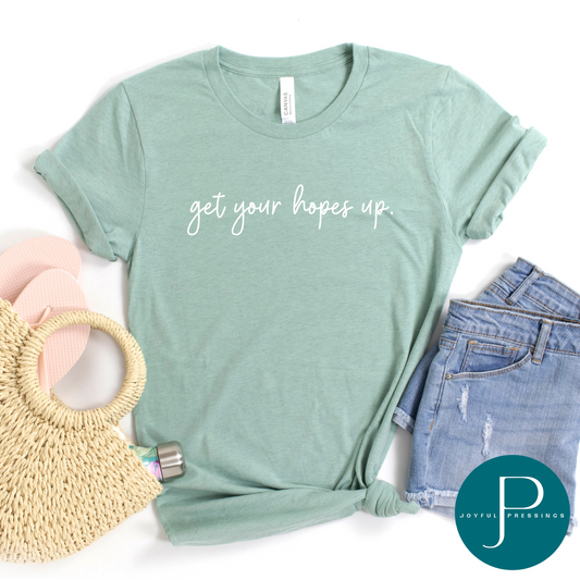 Flatlay of Get your hopes up white print on the front of a light sage green tee.
