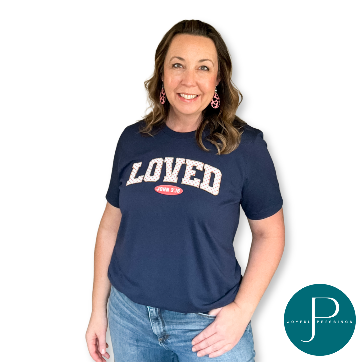 model wearing a navy blue tee with the word loved in white and adorned with pink hearts.  underneath is the reference to the verse John 3:16