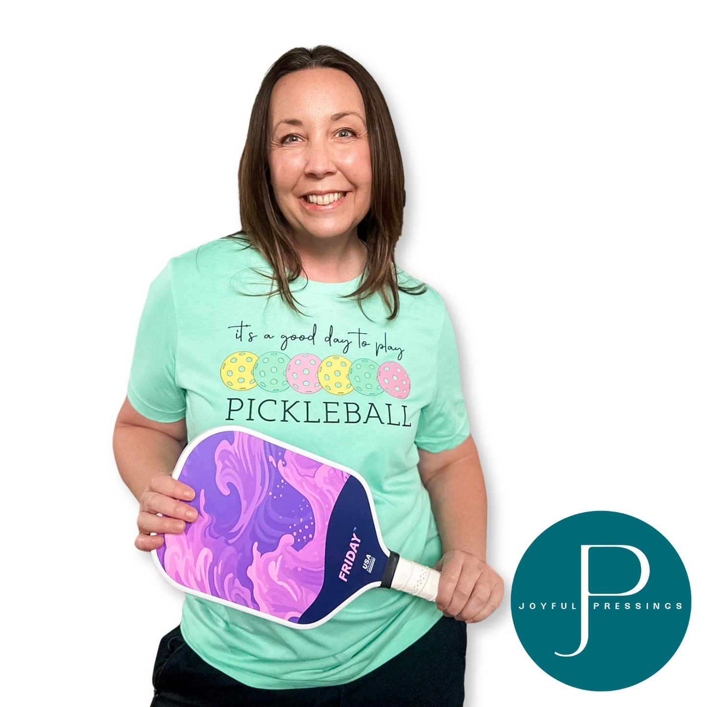 Woman wearing a pickleball-themed shirt and holding a pickleball paddle with a visible brand logo.