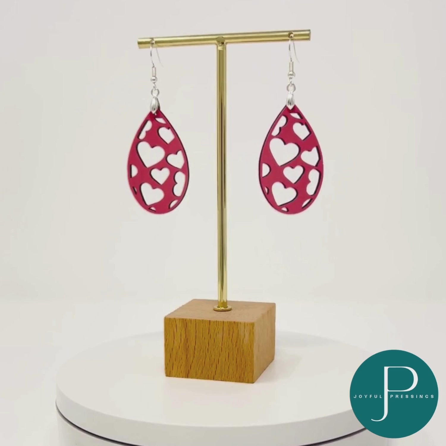pink heart cutout teardrop earrings displayed on a stand rotating in a video