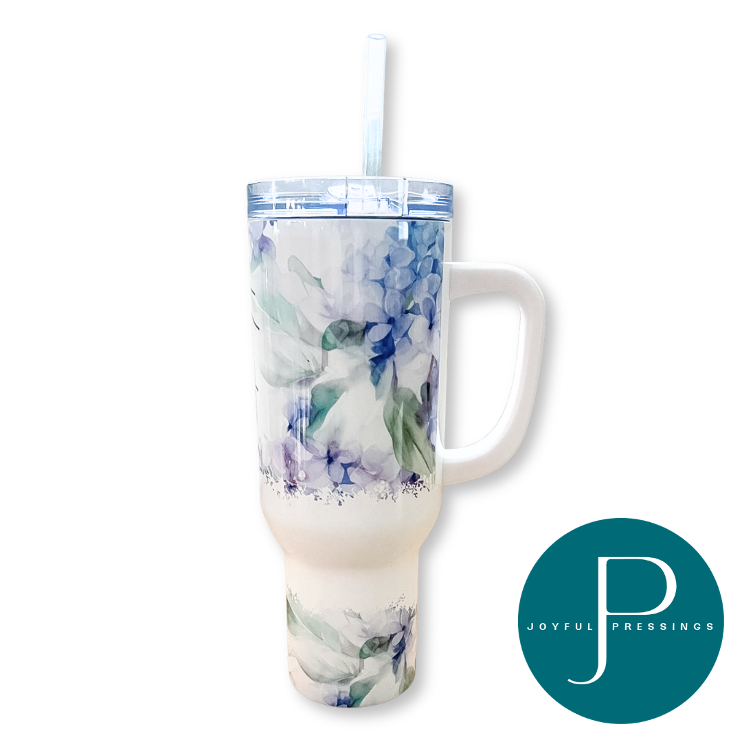 A tall handled tumbler with a clear lid and straw, featuring a watercolor floral print in shades of blue, purple, and green on a white base. A teal circular 'JOYFUL PRESSINGS' logo is shown in the bottom right corner.