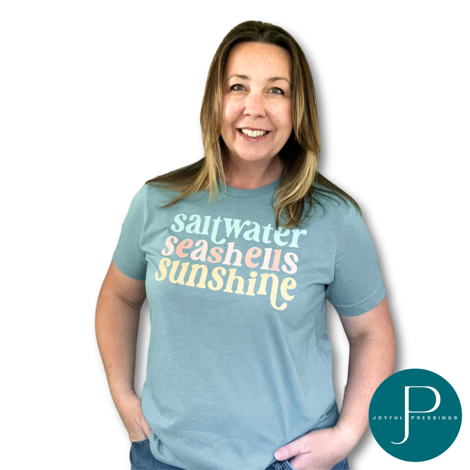 Smiling woman wearing a heather blue lagoon t-shirt with the phrase "saltwater seashells sunshine" in pastel mint, coral, and yellow retro-style lettering.