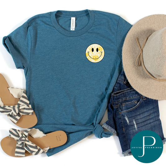 Smiles in Bloom sunflower smiley face graphic tee in heather deep teal by Joyful Pressings, styled with denim shorts, sandals, and a tan hat.